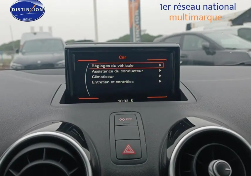 Écran multifonction au centre du tableau de bord d'une Audi A1 blanche, vue intérieure frontale rapprochée.