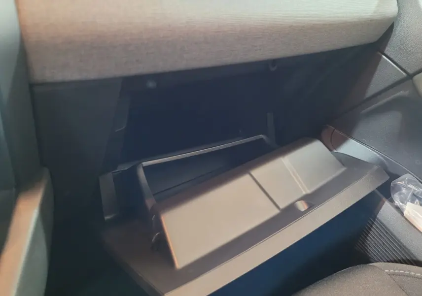 Gros plan sur la boîte à gants ouverte côté passager de la Renault Clio gris foncé, intérieur tissu et plastique.