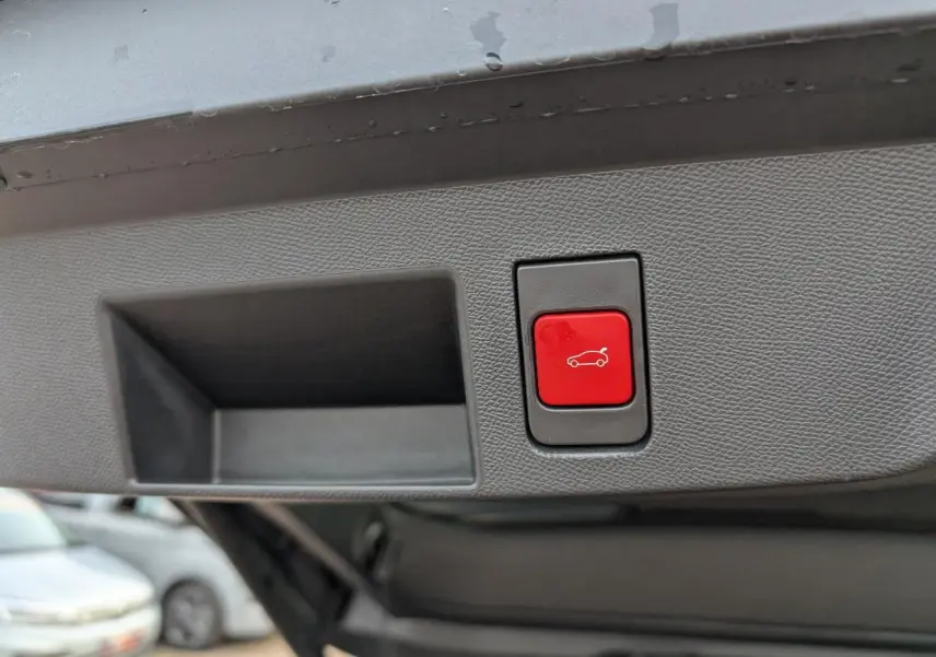 Bouton rouge d'ouverture électrique du hayon sur le panneau intérieur du coffre d'un Citroën C5 Aircross gris.