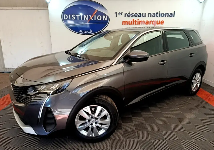 Peugeot 5008 gris clair vue 3/4 avant droit, avec jantes alliage et feux LED, en intérieur showroom.