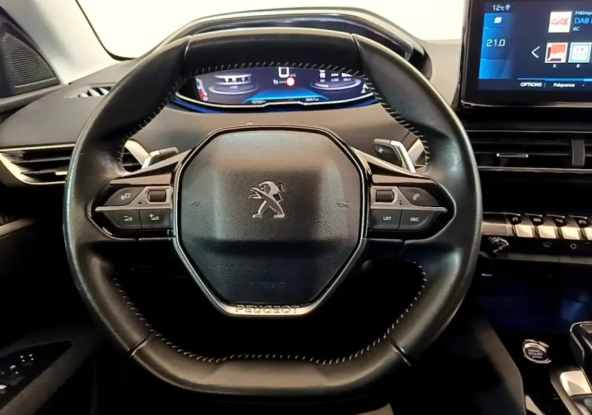 Vue intérieure centrée sur le volant cuir noir du Peugeot 5008 2021 avec tableau de bord numérique et écran tactile.