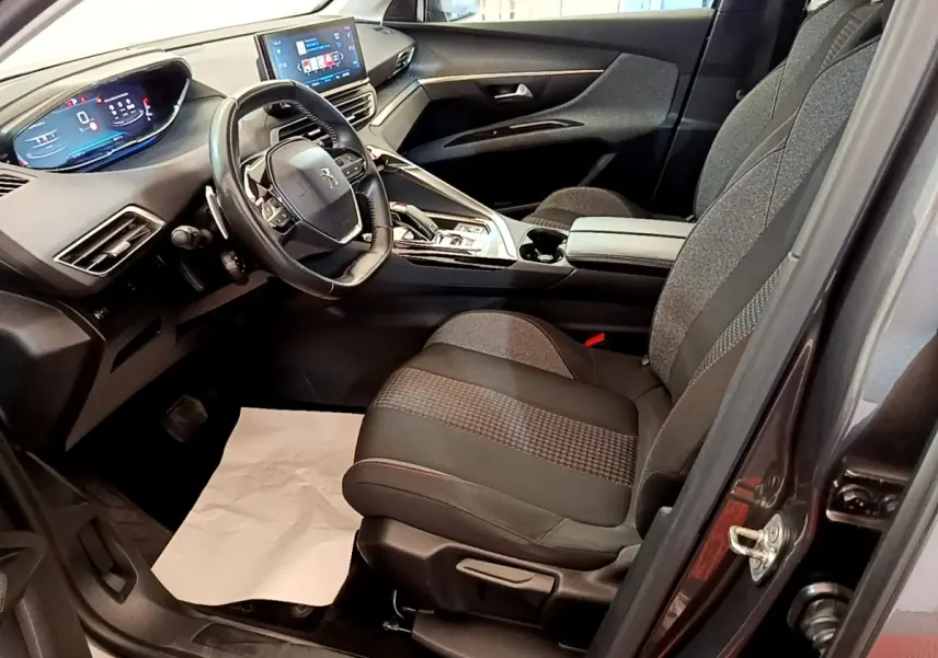 Vue intérieure côté conducteur du Peugeot 5008 gris clair, mettant en valeur le volant cuir et l'écran tactile central.