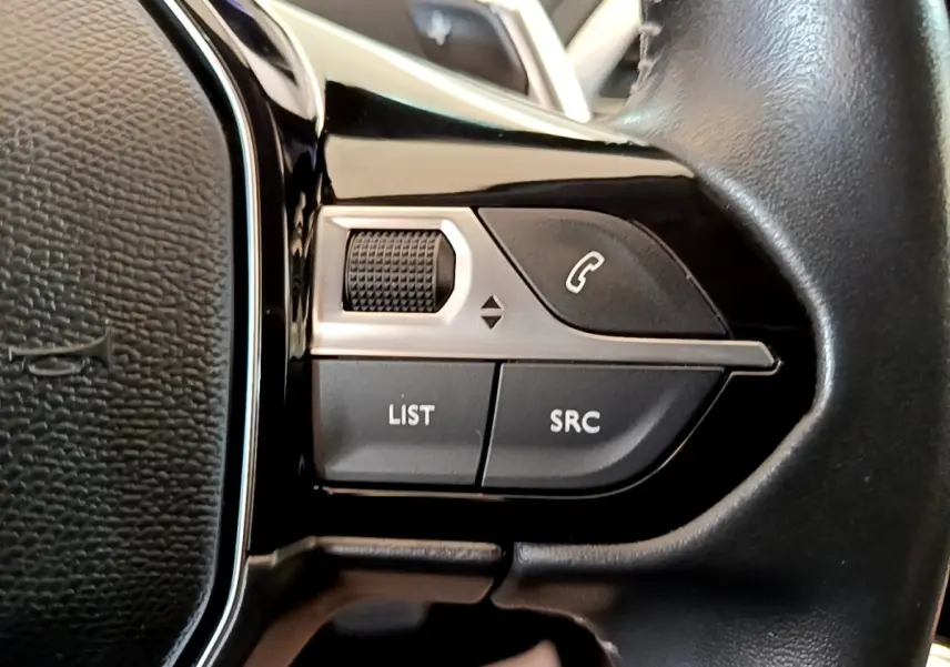 Gros plan sur les commandes gauche du volant cuir noir du Peugeot 5008 gris clair, boutons multifonctions visibles.