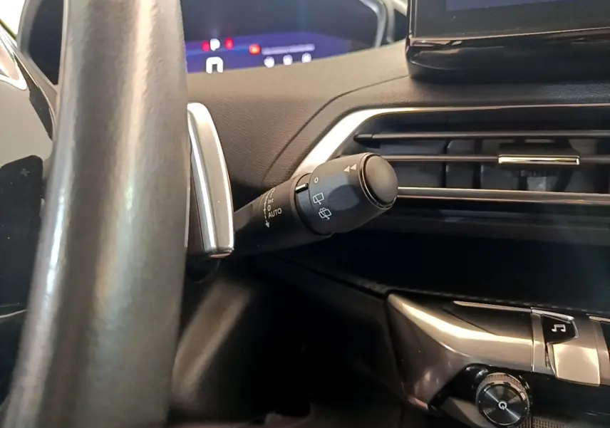 Gros plan sur la commande d’essuie-glace à gauche du volant cuir dans l’habitacle sombre d’un Peugeot 5008 gris clair.