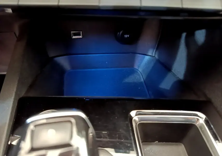 Gros plan sur la console centrale du Peugeot 5008 2021, montrant prise USB, prise 12V et rangement noir brillant.