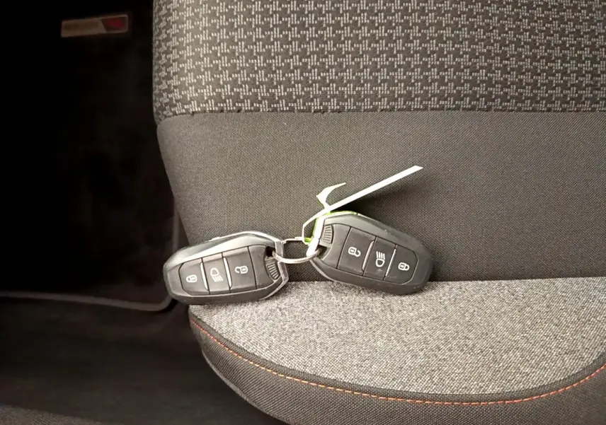 Gros plan sur deux clés de voiture noires posées sur un siège tissu gris à surpiqûres orange du Peugeot 5008.