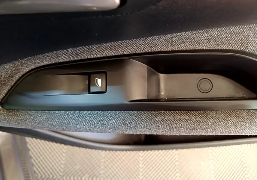 Gros plan sur la poignée intérieure de porte avec bouton de verrouillage, tissu gris clair visible autour.