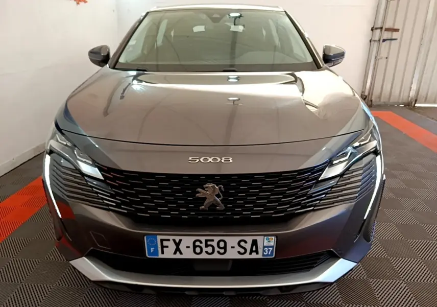 Peugeot 5008 gris clair vue de face, avec calandre noire et phares LED allumés dans un garage.