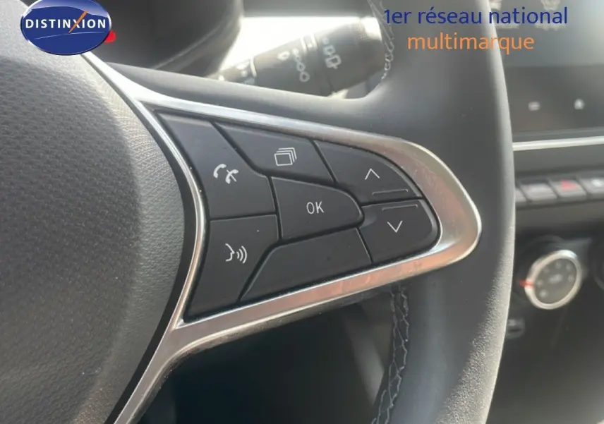 Gros plan sur les commandes multifonctions à droite du volant d’une Renault Clio blanche, intérieur noir avec coutures visibles.