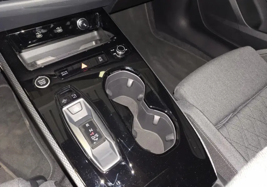 Vue rapprochée de la console centrale noire brillante de l'Audi A5 Avant 2025 avec levier de vitesse automatique et porte-gobelets.