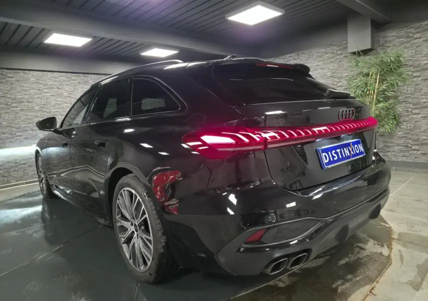 Audi A5 Avant noir vue 3/4 arrière droit en intérieur, feux arrière LED allumés et jantes 19 pouces visibles.