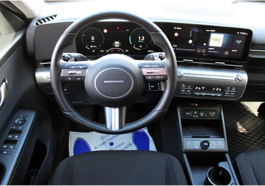 Vue intérieure frontale du tableau de bord et volant cuir du Hyundai Kona 2024 avec écran tactile panoramique.