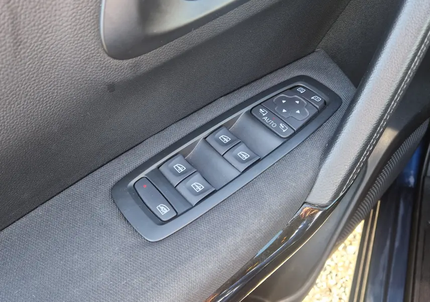 Gros plan sur les commandes des vitres électriques et réglages des rétroviseurs côté conducteur d’un Renault Kadjar bleu cosmos.