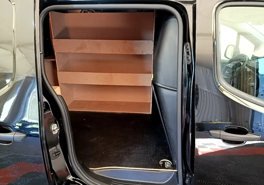 Vue latérale du Peugeot Partner noir 2022 avec porte coulissante ouverte montrant l'aménagement intérieur avec étagères en bois.