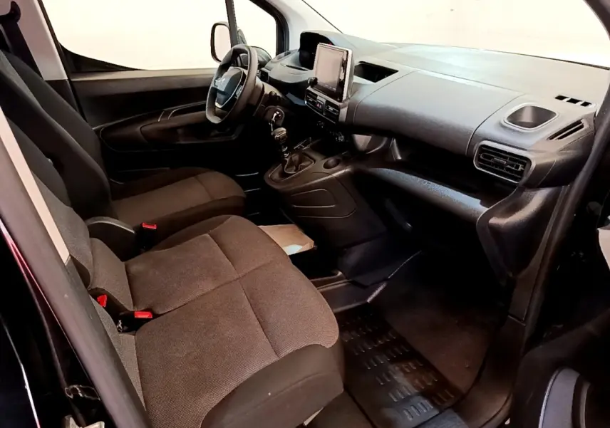 Vue intérieure côté conducteur du Peugeot Partner 2022 noir, montrant le tableau de bord et les sièges avant en tissu.