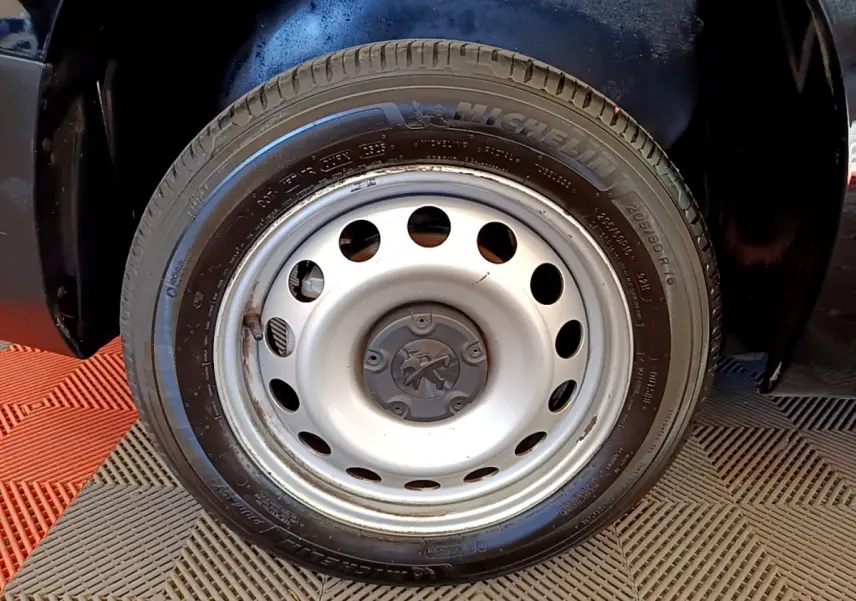 Gros plan sur la roue avant droite en jante acier argentée du Peugeot Partner noir, pneu Michelin visible.