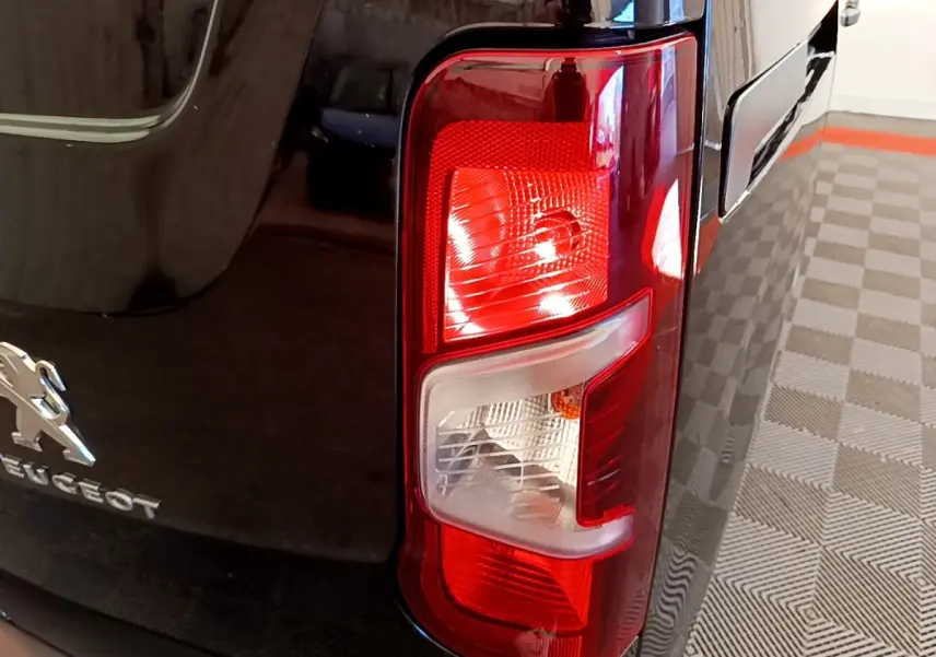 Gros plan sur le feu arrière droit rouge et blanc d’un Peugeot Partner noir, avec logo visible sur la carrosserie.