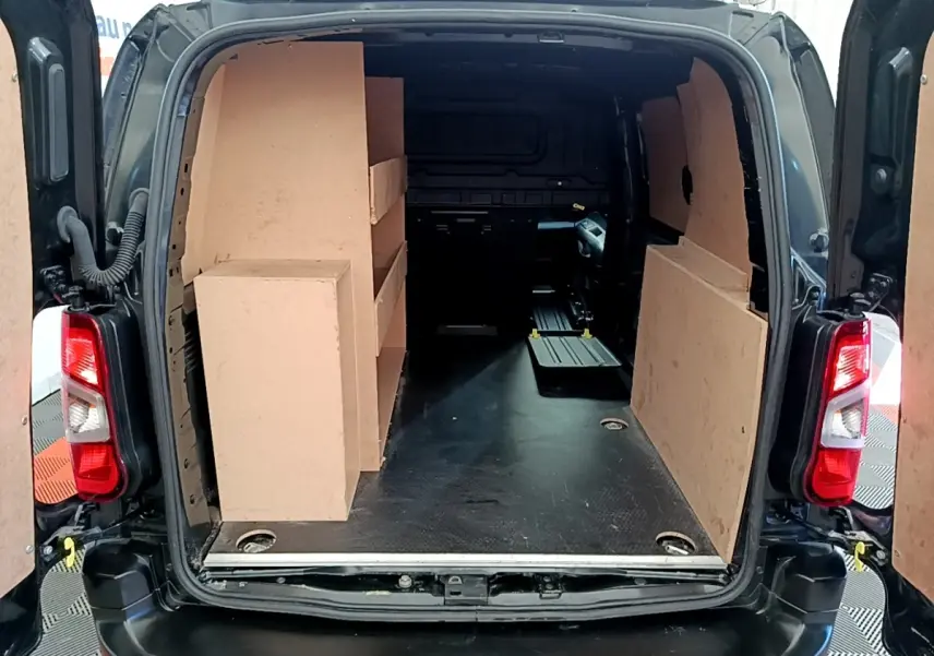 Vue arrière ouverte du Peugeot Partner noir 2022, montrant l'espace de chargement avec cloison et étagères en bois.
