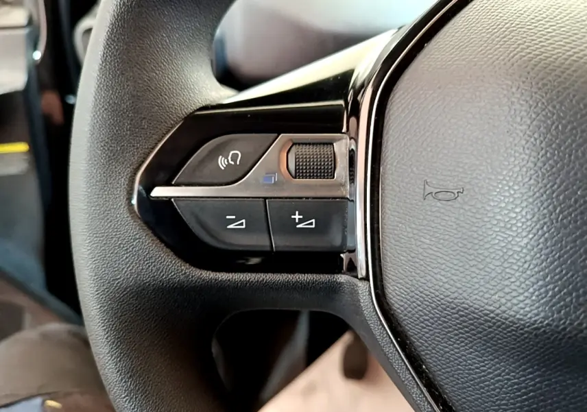 Gros plan sur les commandes gauche du volant noir du Peugeot Partner 2022, avec boutons de volume et appel mains libres.