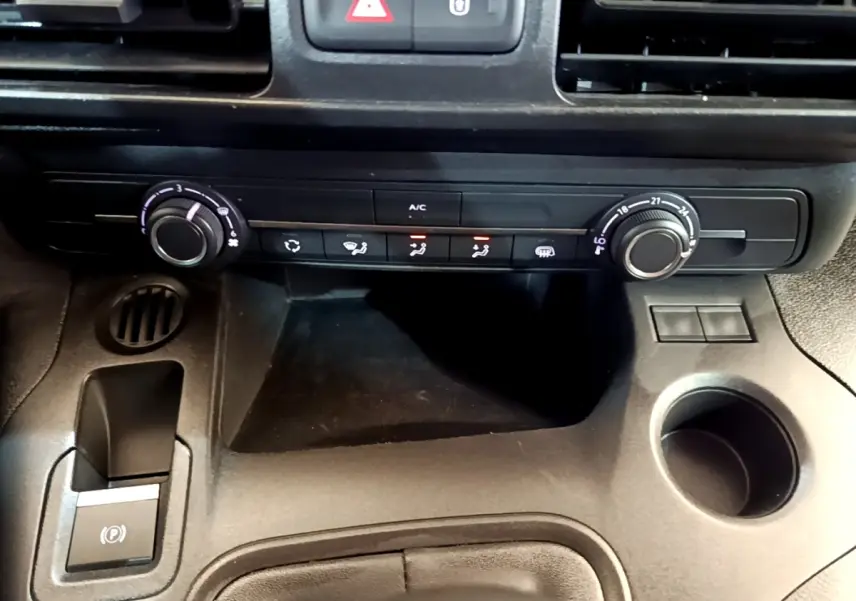 Vue rapprochée de la console centrale noire du Peugeot Partner 2022, montrant les commandes de climatisation et frein à main électrique.