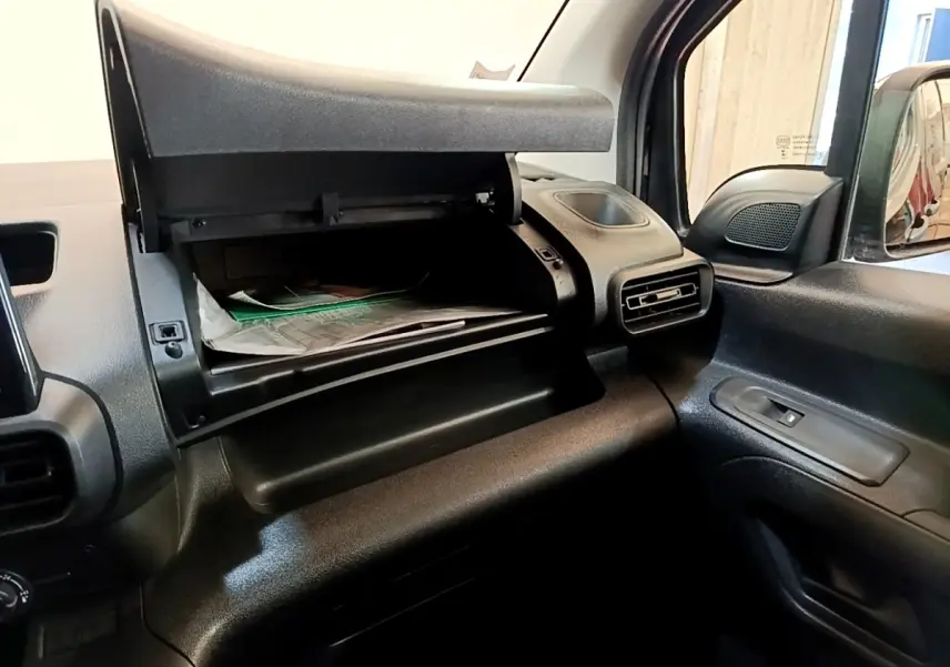 Vue intérieure du compartiment à gants ouvert côté passager du Peugeot Partner noir, montrant la console et la ventilation.