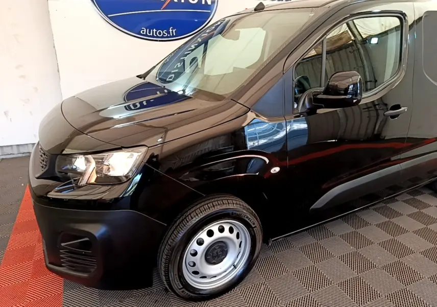 Vue 3/4 avant droit du Peugeot Partner noir avec jante acier et phares allumés en intérieur showroom.