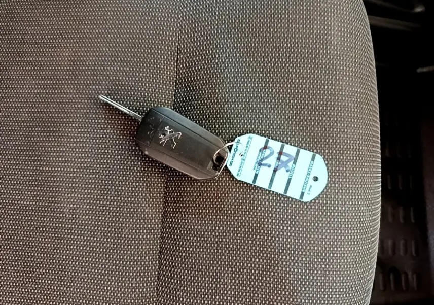Clé de voiture Peugeot posée sur un siège tissu gris foncé à motifs fins à l'intérieur du véhicule.