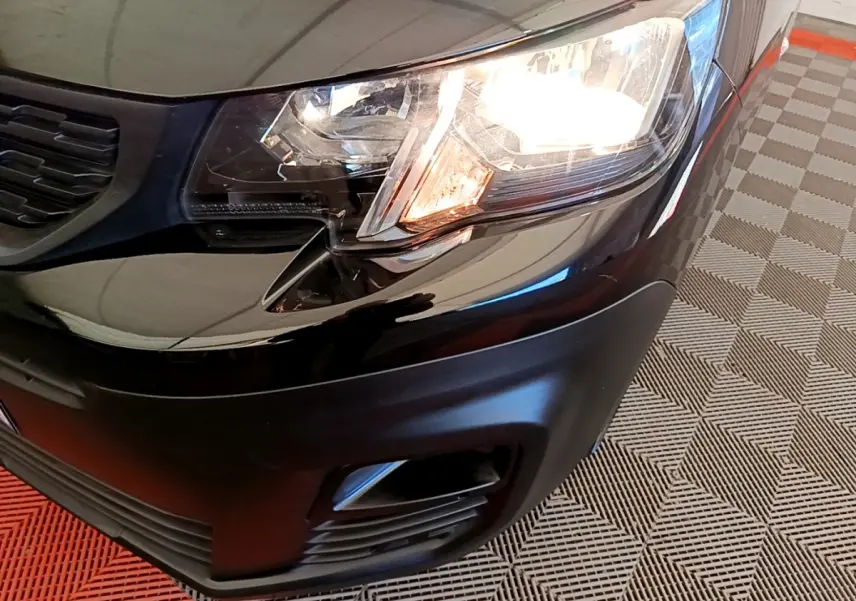 Gros plan sur l'avant droit noir du Peugeot Partner 2022 avec phare allumé et antibrouillard intégré.