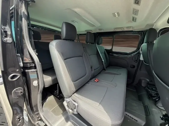 Vue intérieure côté gauche du Nissan Primastar noir 2025, montrant les sièges passagers arrière et la porte latérale ouverte.