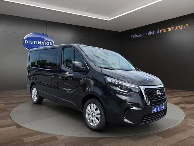 Nissan Primastar noir en 3/4 avant droit, avec calandre chromée et feux LED, sur fond intérieur showroom.