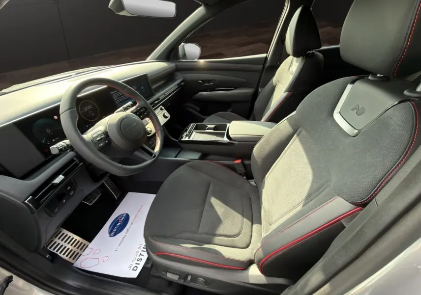 Vue intérieure côté conducteur du Hyundai Tucson 1.6 Hybrid N Line gris clair, sièges sport avec surpiqûres rouges et tableau de bord numérique.