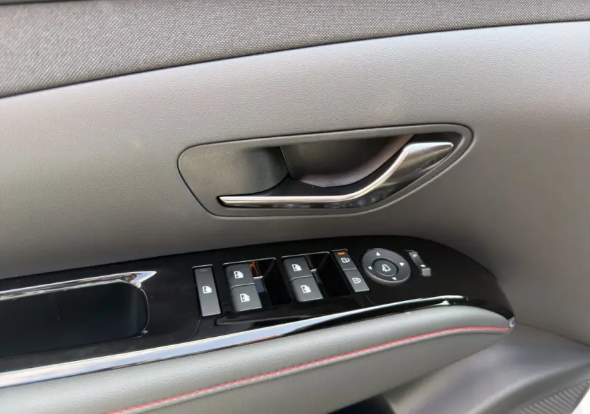 Gros plan sur la poignée de porte intérieure gris clair et les commandes électriques des vitres du Hyundai Tucson 1.6 Hybrid N Line 2026.