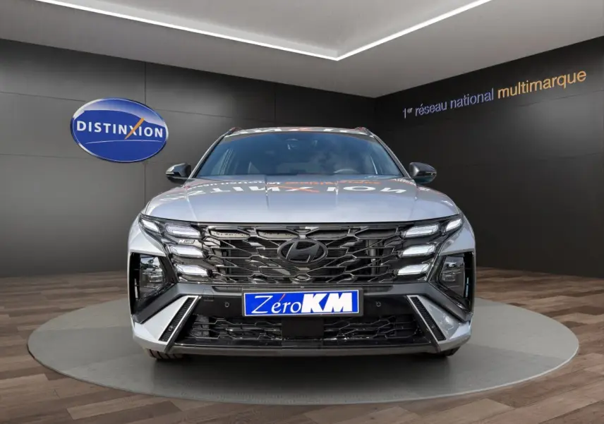 Vue frontale d'un Hyundai Tucson gris clair 2026 avec calandre noire et éclairage LED distinctif en showroom.