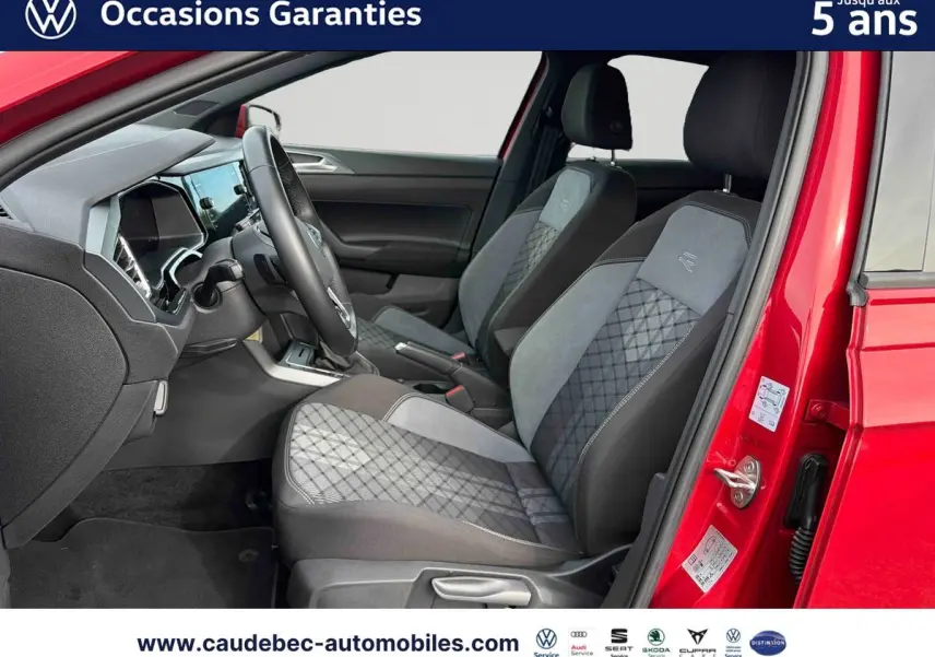Vue intérieure côté conducteur d'une Volkswagen Polo rouge 2025, sièges avant tissu gris à motifs et volant cuir multifonctions.