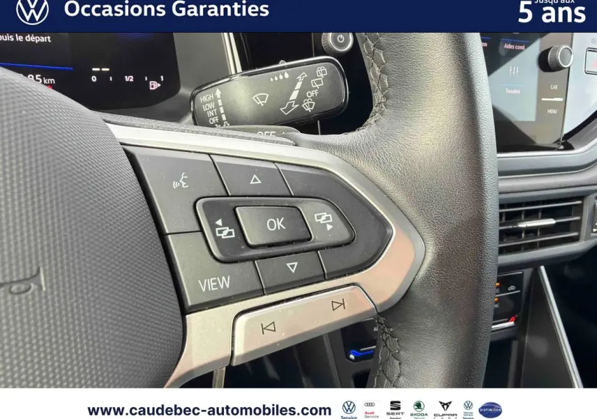 Gros plan sur les commandes multifonctions du volant cuir noir du Volkswagen Polo rouge, avec tableau de bord digital en arrière-plan.