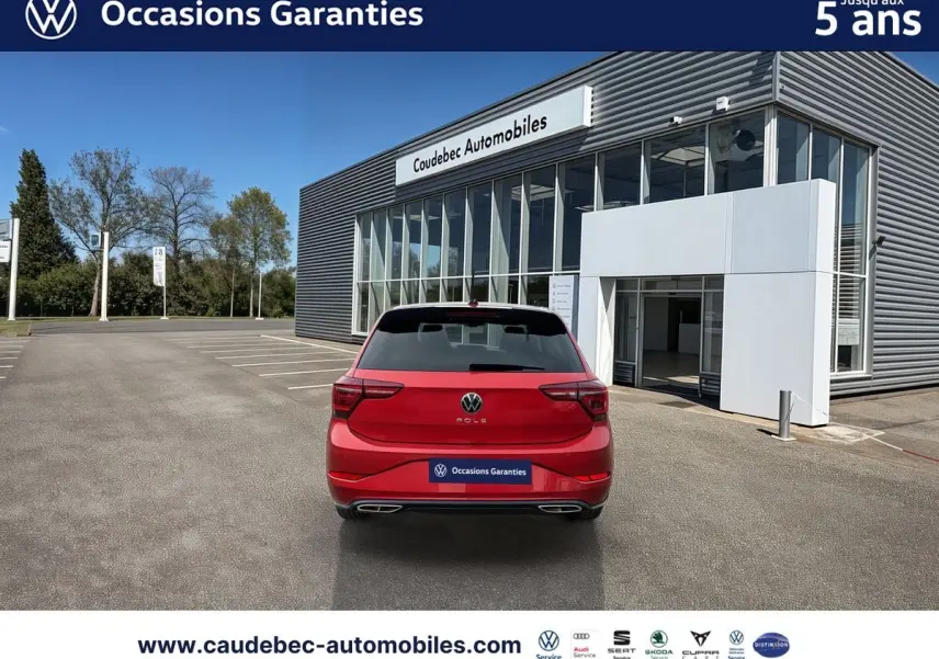 Vue arrière d'une Volkswagen Polo rouge 2025 garée devant un bâtiment moderne de concession automobile.