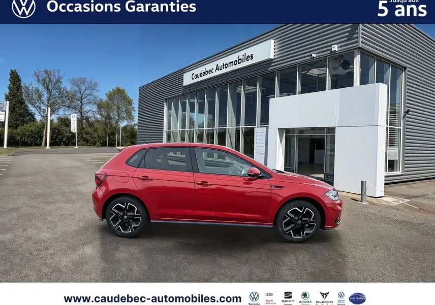 Profil droit d'une Volkswagen Polo rouge 2025 garée devant un bâtiment moderne de concession automobile.