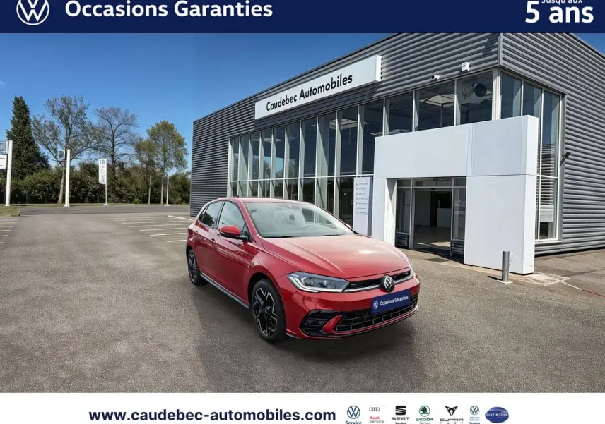Volkswagen Polo rouge vue 3/4 avant droit, avec jantes alliage noires, stationnée devant un bâtiment moderne.