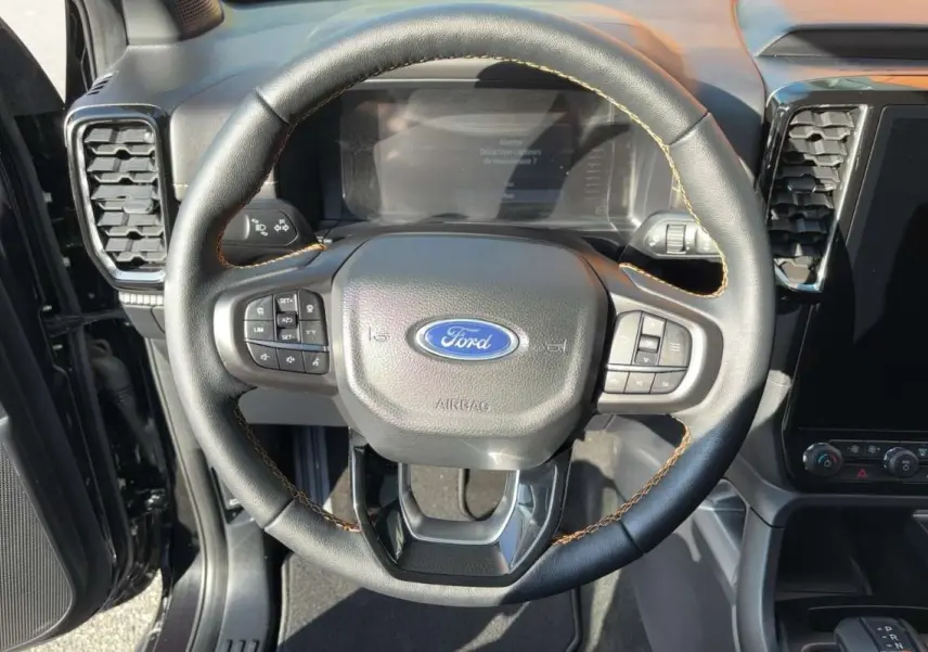 Vue rapprochée du volant cuir noir avec surpiqûres marron du Ford Ranger Wildtrak 2026, tableau de bord et écran tactile visibles.