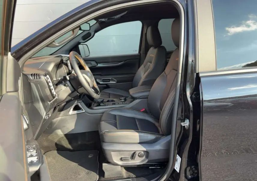 Vue intérieure côté conducteur du Ford Ranger noir agate, sièges en cuir avec surpiqûres orange et volant multifonctions.