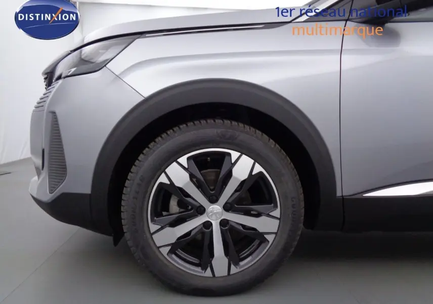 Gros plan sur la roue avant gauche et l'aile d'un Peugeot 3008 gris Artense métal, finition Allure Pack 2023.