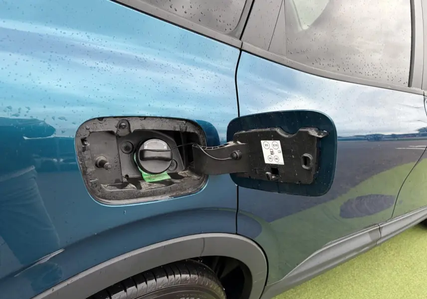 Gros plan sur la trappe à carburant ouverte côté gauche d'une Renault Arkana bleu Zanzibar métallisé.