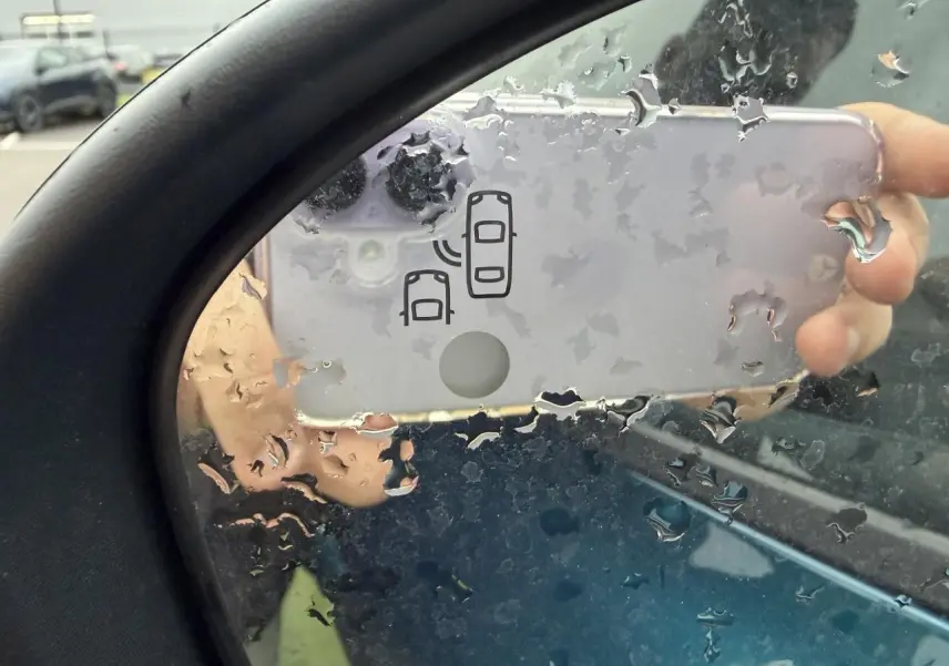 Rétroviseur côté gauche d'un Renault Arkana bleu Zanzibar, avec icône d'alerte d'angle mort visible sous la pluie.