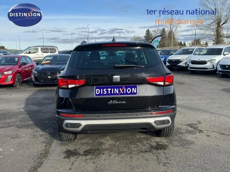 Vue arrière d'un SEAT Ateca noir métallique garé sur un parking avec plusieurs autres véhicules autour.