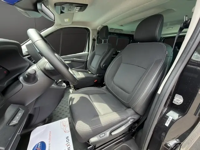 Vue intérieure côté conducteur du Nissan Primastar noir 2025, montrant les sièges avant en tissu et le volant multifonctions.