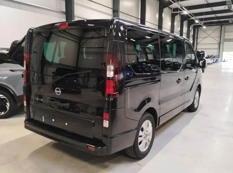 Vue 3/4 arrière droite d’un Nissan Primastar noir avec portes latérales et vitres teintées dans un garage.