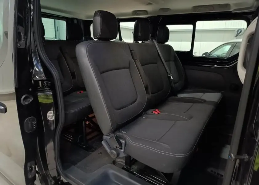 Vue intérieure côté droit du Nissan Primastar noir, montrant les sièges passagers en tissu et la porte latérale ouverte.