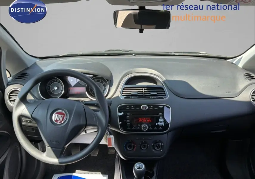 Vue intérieure frontale du tableau de bord gris foncé de la Fiat Punto Street 2016 avec volant, radio et levier de vitesse manuel.
