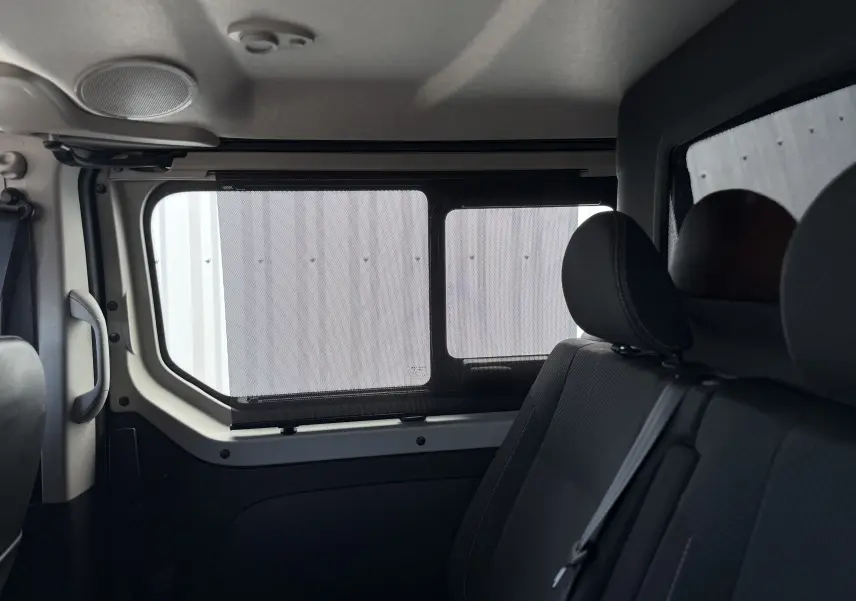 Vue intérieure côté droit sur les sièges arrière gris du Renault Trafic Cabine Approfondie avec store pare-soleil sur la fenêtre.