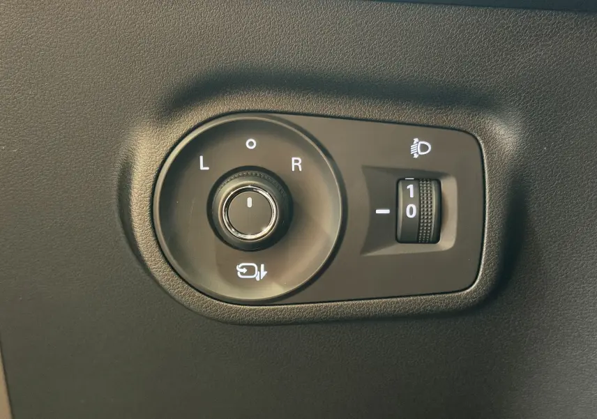 Gros plan sur la commande de réglage des rétroviseurs et des phares du MG MOTOR ZS 2026 en intérieur noir.